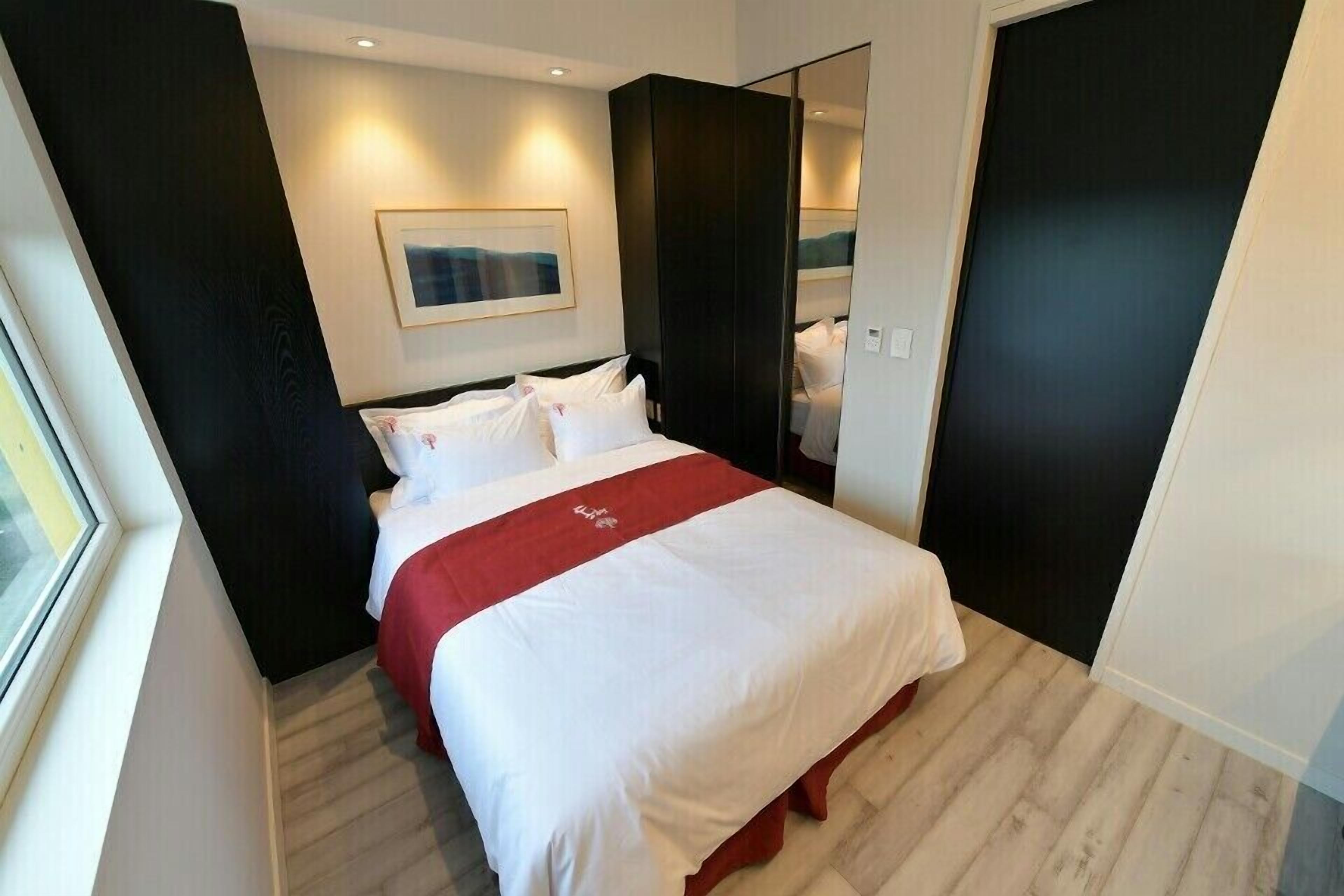 Une chambre d’hôtel moderne avec un grand lit, une couvre-lit rouge et blanche, un tableau encadré au mur et un grand miroir.