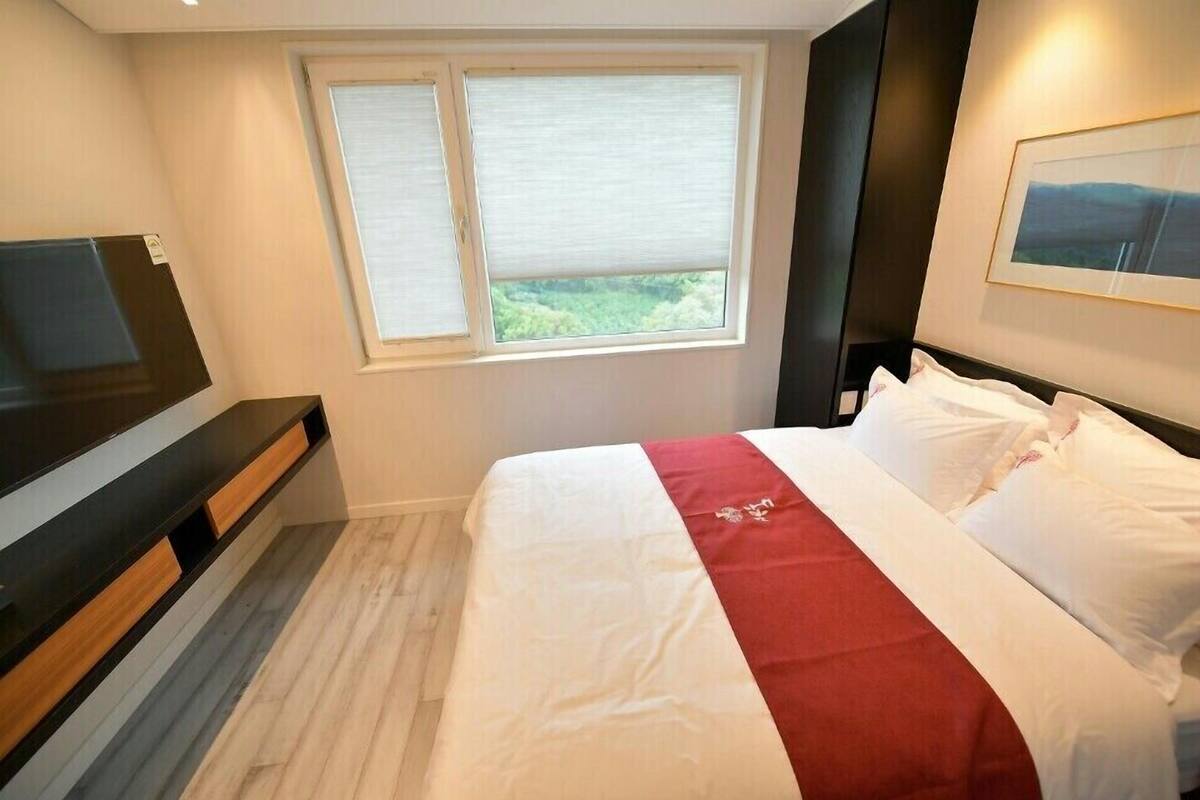 A hotel room with a bed, a TV, a window with a view, and a painting on the wall.