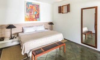 Habitación de hotel con una cama, dos lámparas de noche, un banco de madera, un espejo grande y un cuadro abstracto colorido en la pared.