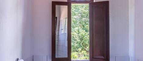 A bathroom with a large mirror, a white sink, and a window with an open wooden door.