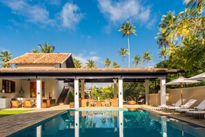 A poolside area with a covered seating area, lounge chairs, and palm trees. - Nyne Hotels The Muse - Bentota (Bentota)