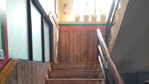 A wooden staircase with a handrail, leading to a landing with a window and potted plants. - Hotel Grand Shambala (Muktinath)