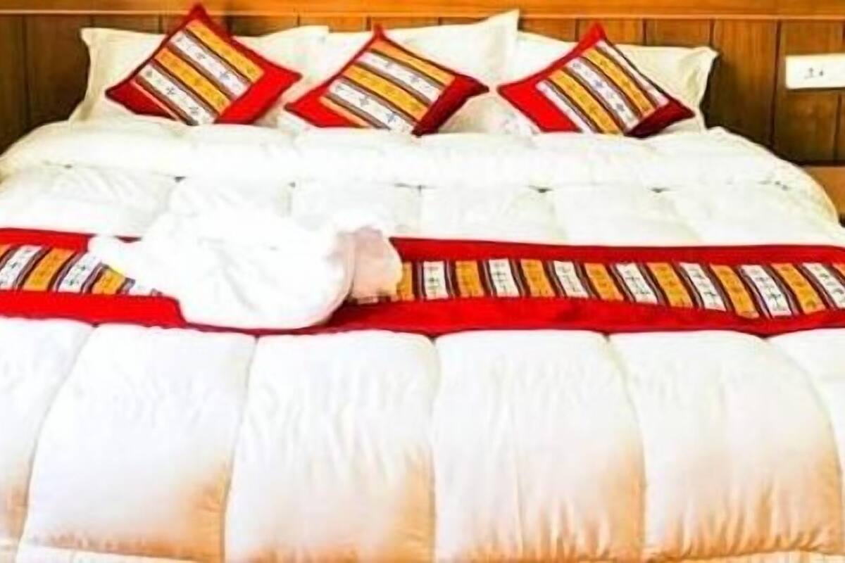 A bed with a white duvet and red and yellow striped pillows, a wooden headboard, and a nightstand with a lamp.
