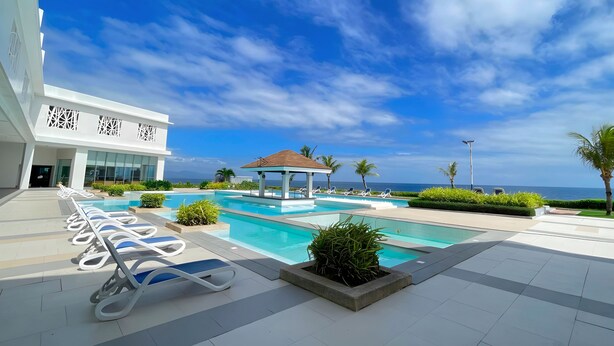 A modern pool area with lounge chairs, a gazebo, and a view of the ocean. - Arterra Hotel and Resort (Lapu-Lapu)