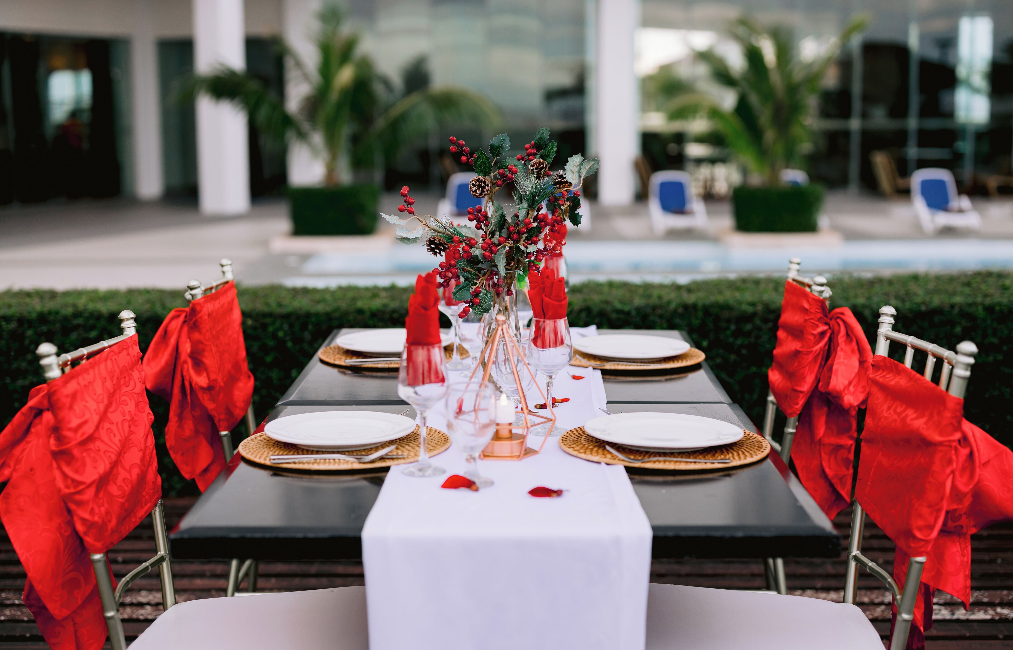 A table set for a meal with red napkins, white tablecloth, and a centerpiece with greenery and pinecones.