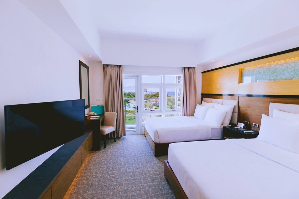 Ein Hotelzimmer mit zwei Betten, einem Fernseher, einem Schreibtisch und Blick ins Freie.