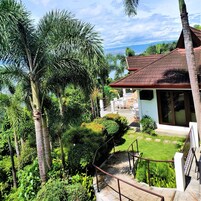 Un jardín tropical con palmeras y una casa con techo rojo y ventanas grandes.