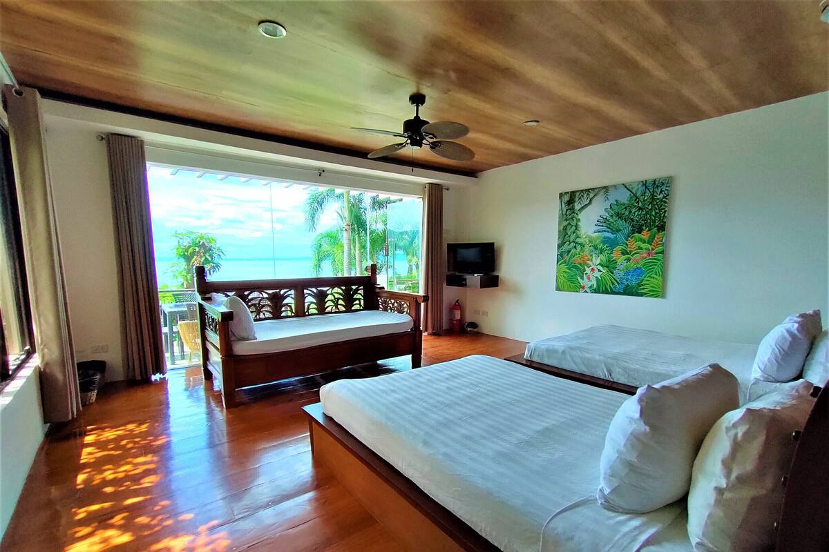 A hotel room with two beds, a ceiling fan, a painting, and a view of the ocean.