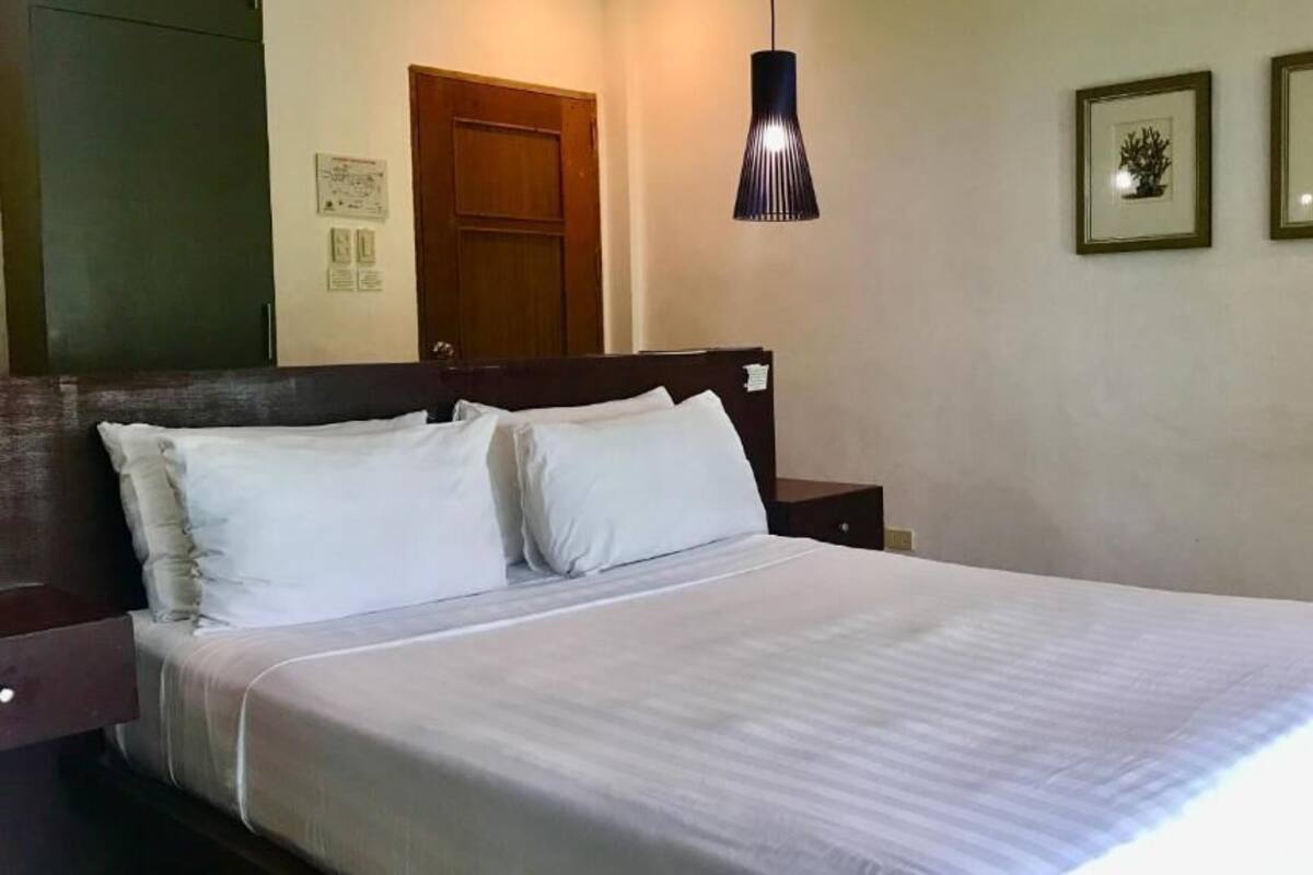 A bed with white bedding, a wooden headboard, a nightstand, a hanging lamp, and two framed pictures on the wall.