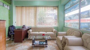 Habitación con sofá, una mesita de centro, escritorio y silla. Se ve una ventana con persianas y vistas al exterior.