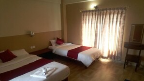 Habitación de hotel con dos camas, cada una con ropa de cama blanca y detalles en rojo, piso de madera, un escritorio con silla y una ventana con cortinas translúcidas.