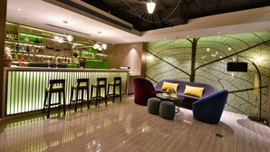 A modern bar area with a green-lit counter, bar stools, and a seating area with a sofa and ottomans. - ibis Styles XM Zhongshan (Xiamen)