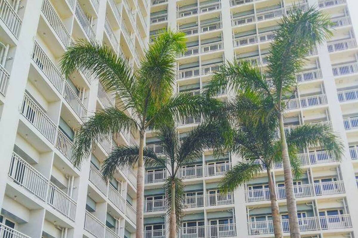 A high-rise building with multiple balconies and a swimming pool area with palm trees.