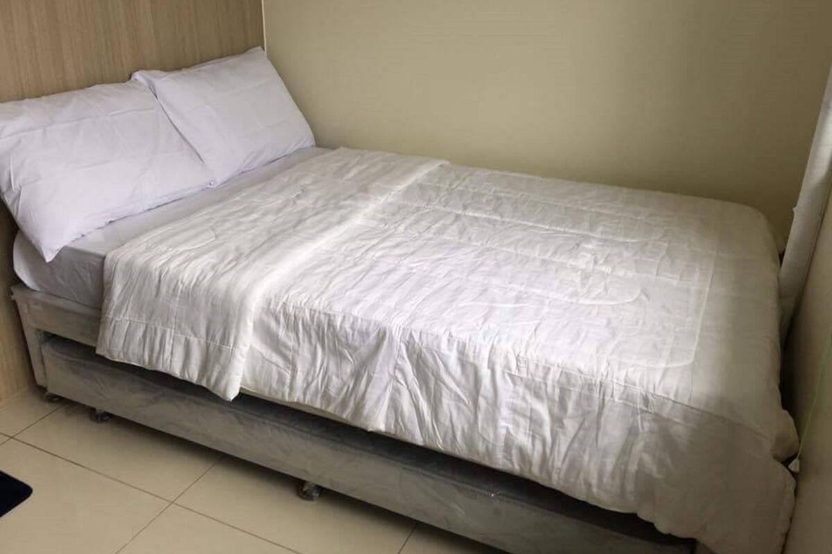 A single bed with a white mattress and bedding, a wooden headboard, and a tiled floor.