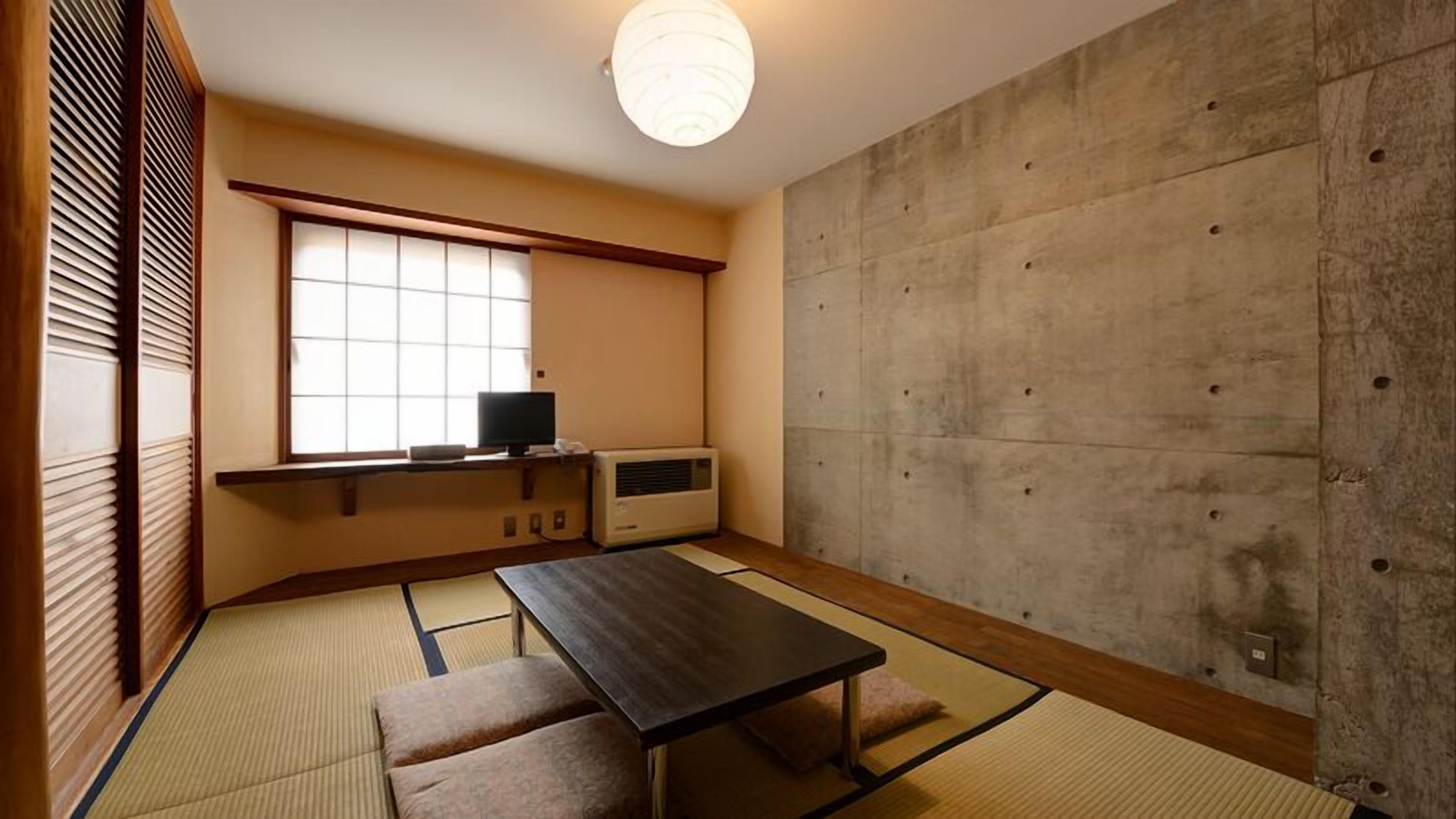 A traditional Japanese room with tatami flooring, a low table, a television, and a concrete wall.