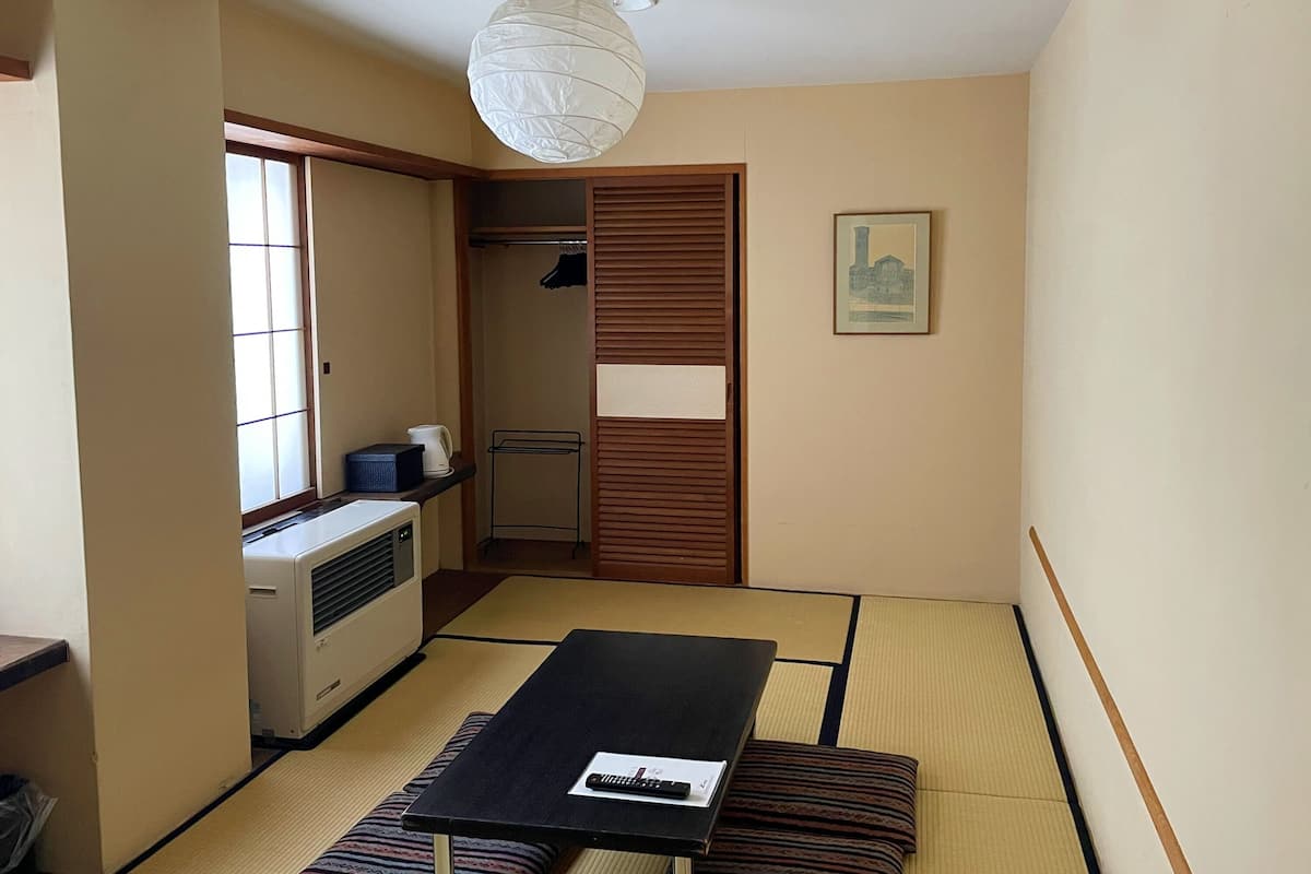A traditional Japanese room with tatami flooring, a black table, a white air conditioner, a hanging light fixture, and a framed picture on the wall.