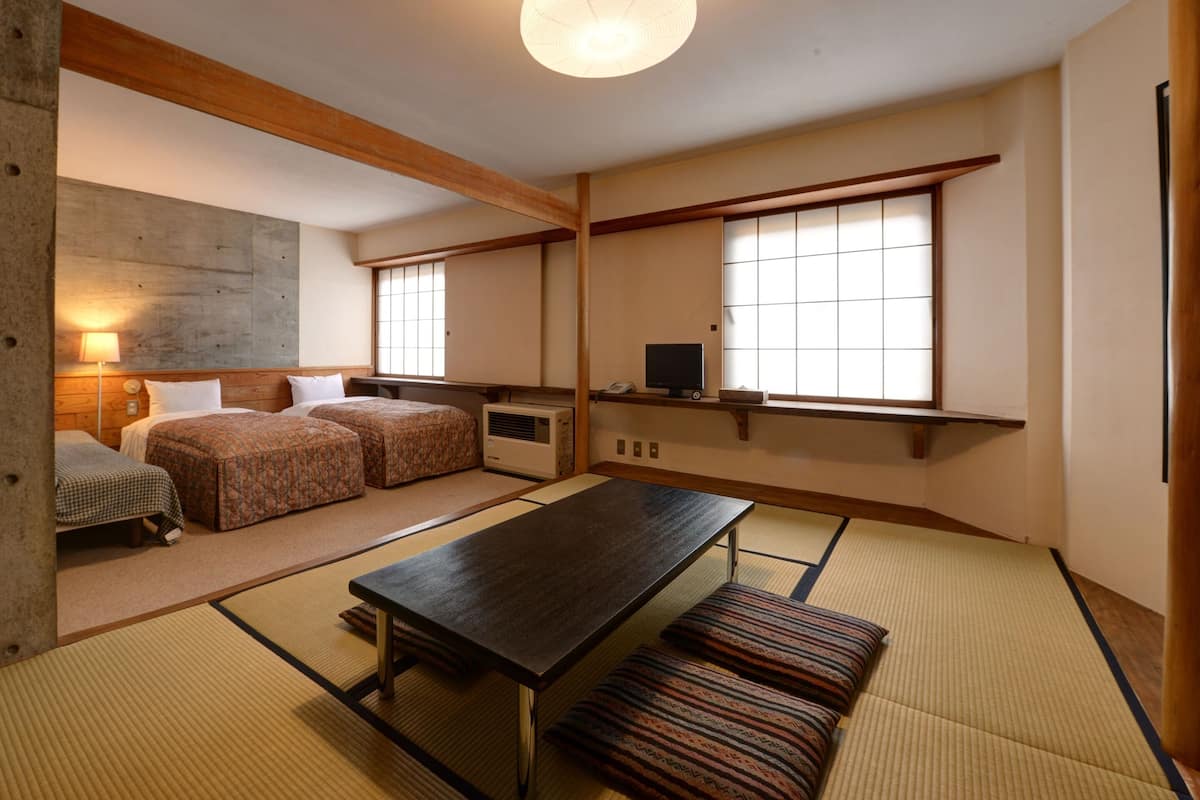 A traditional Japanese-style room with tatami flooring, a low table, two beds, and a large window with shoji screens.
