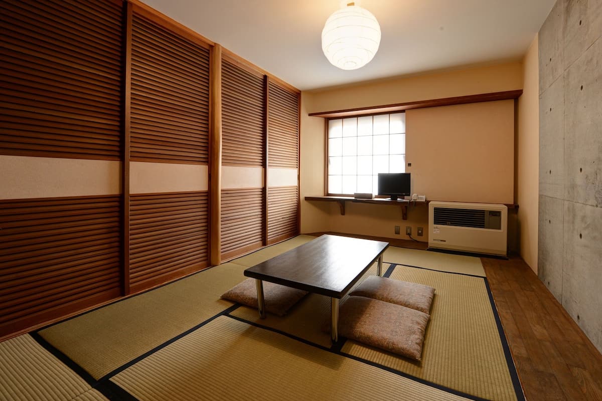 A traditional Japanese room with tatami flooring, a low table, cushions, a television, and a heater.