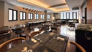 Un comedor amplio con varias mesas y sillas, ventanas grandes y un techo alto con iluminación empotrada.