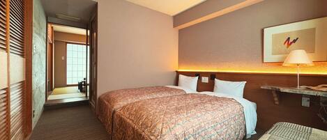 Una habitación de hotel con dos camas, una mesita de noche con lámpara, un televisor de pared y una puerta que da a otra habitación.