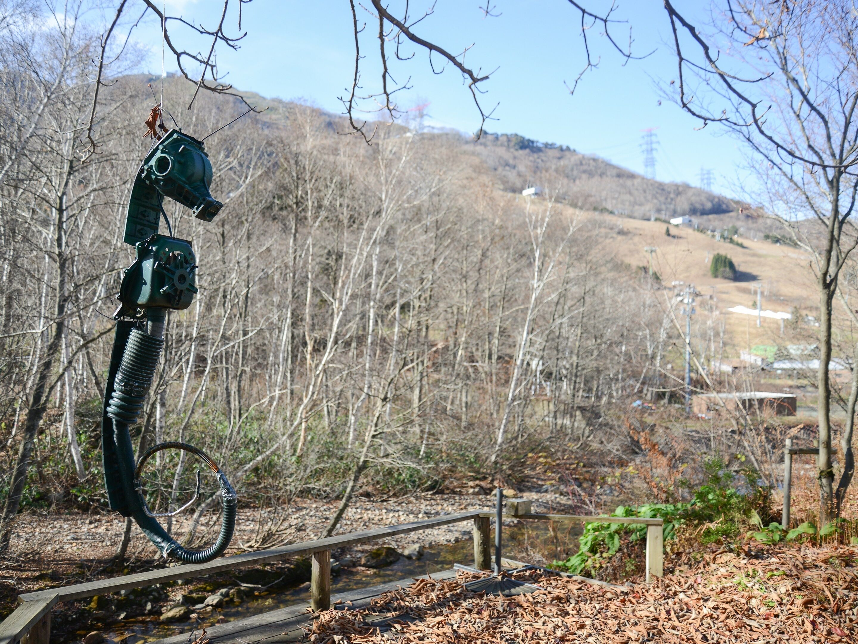 Una escultura de un caballo sobre una estructura metálica en un parque con un puente de madera y suelo cubierto de hojas.