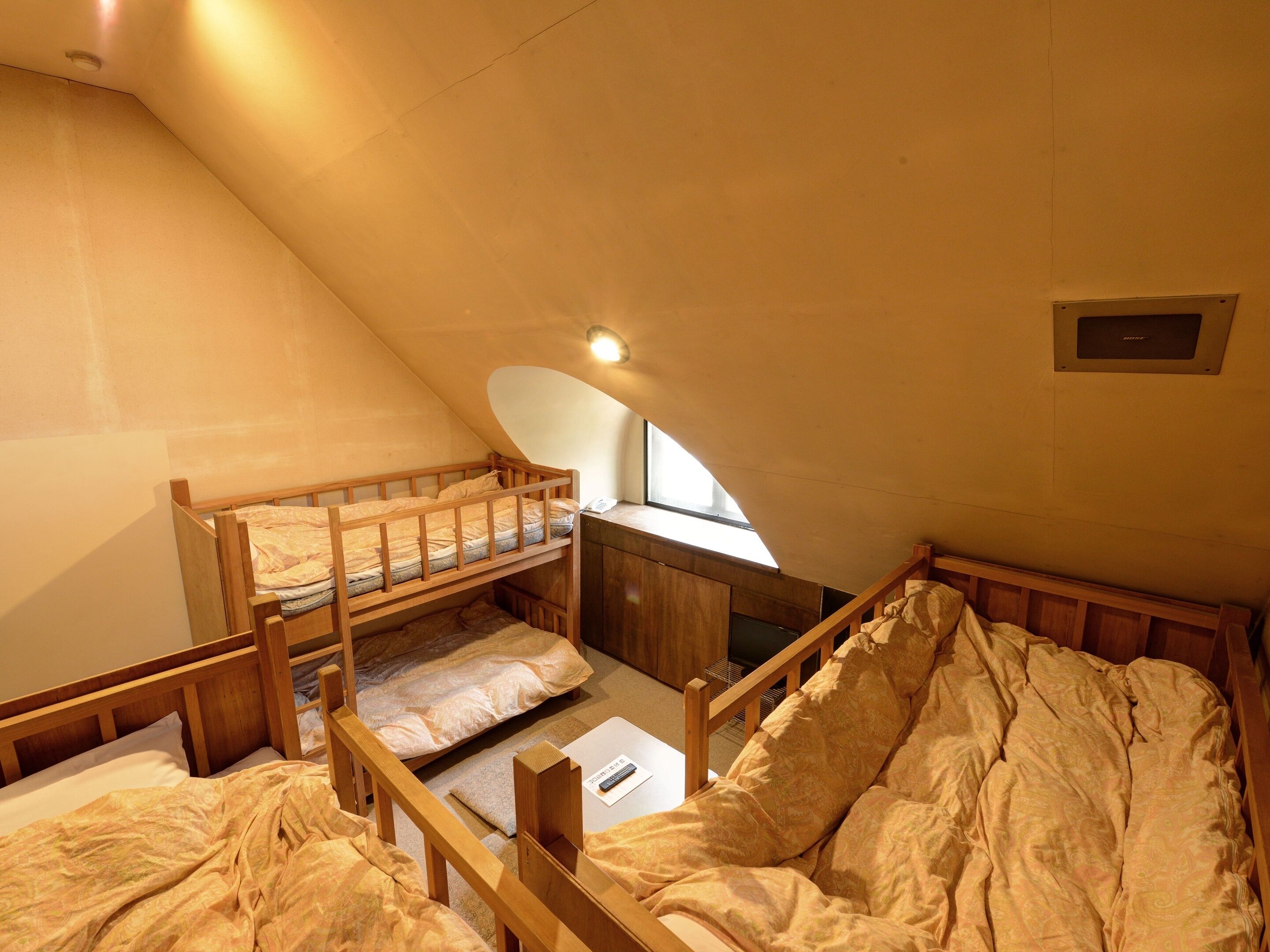 A dormitory room with bunk beds, a desk, and a window.