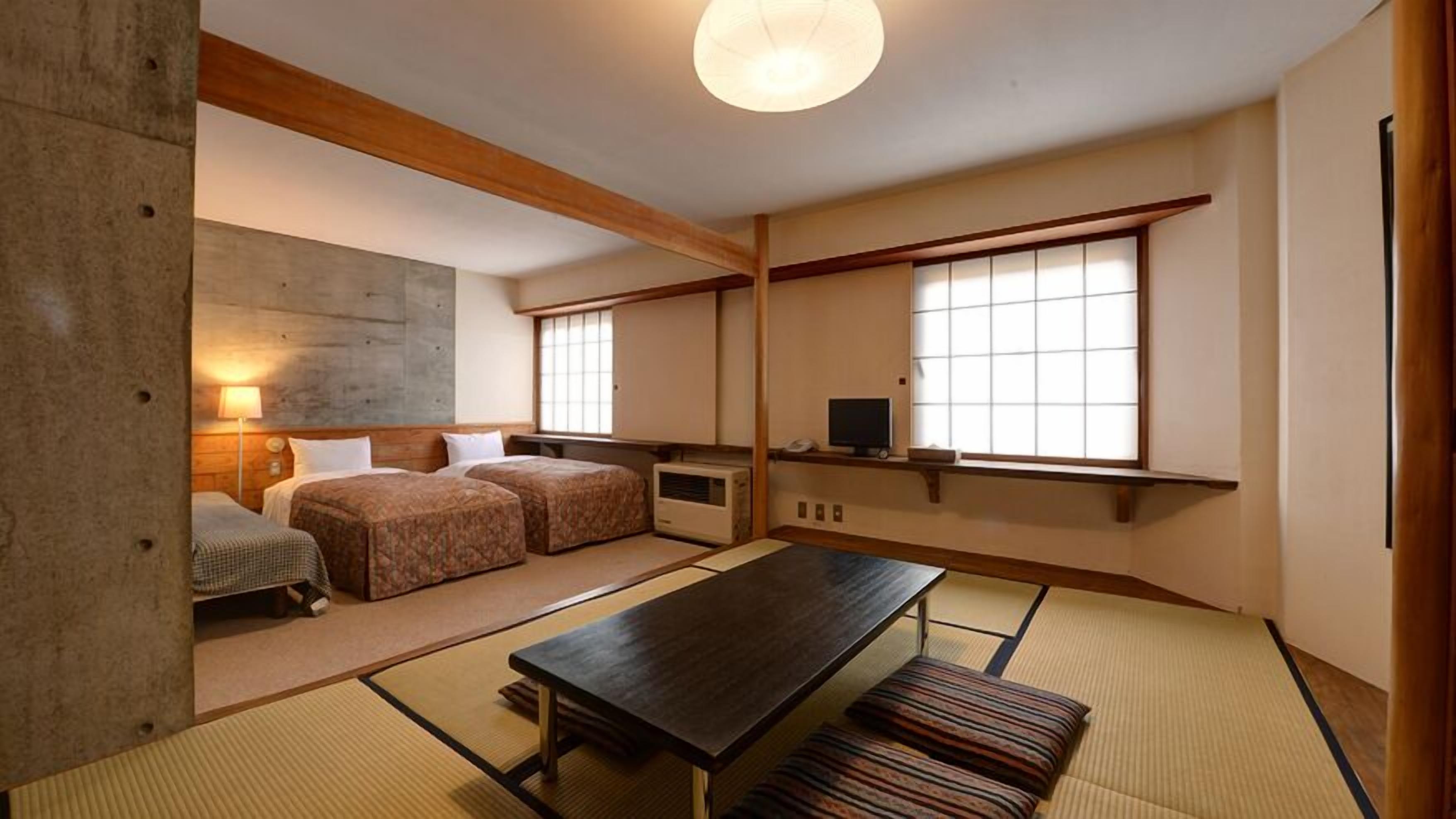 A traditional Japanese room with tatami flooring, a low table, two beds, and a television.