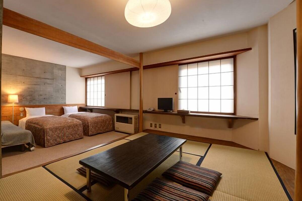 A traditional Japanese room with tatami flooring, a low table, two beds, and a television.
