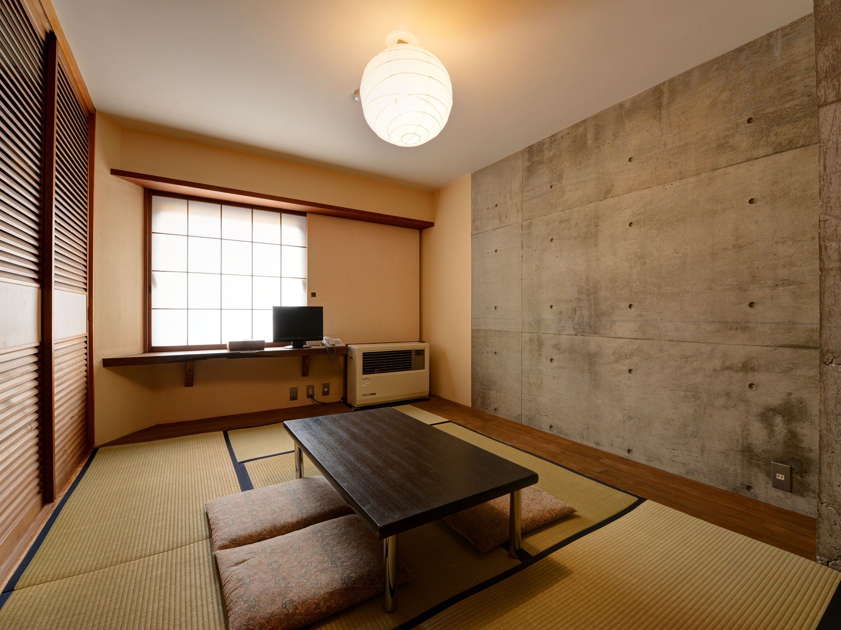 A traditional Japanese room with tatami flooring, a low table, cushions, a television, and a large window.