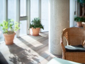 A room with a large window, a concrete pillar, a wicker chair, and potted plants. - the Kinta Naeba (Yuzawa)