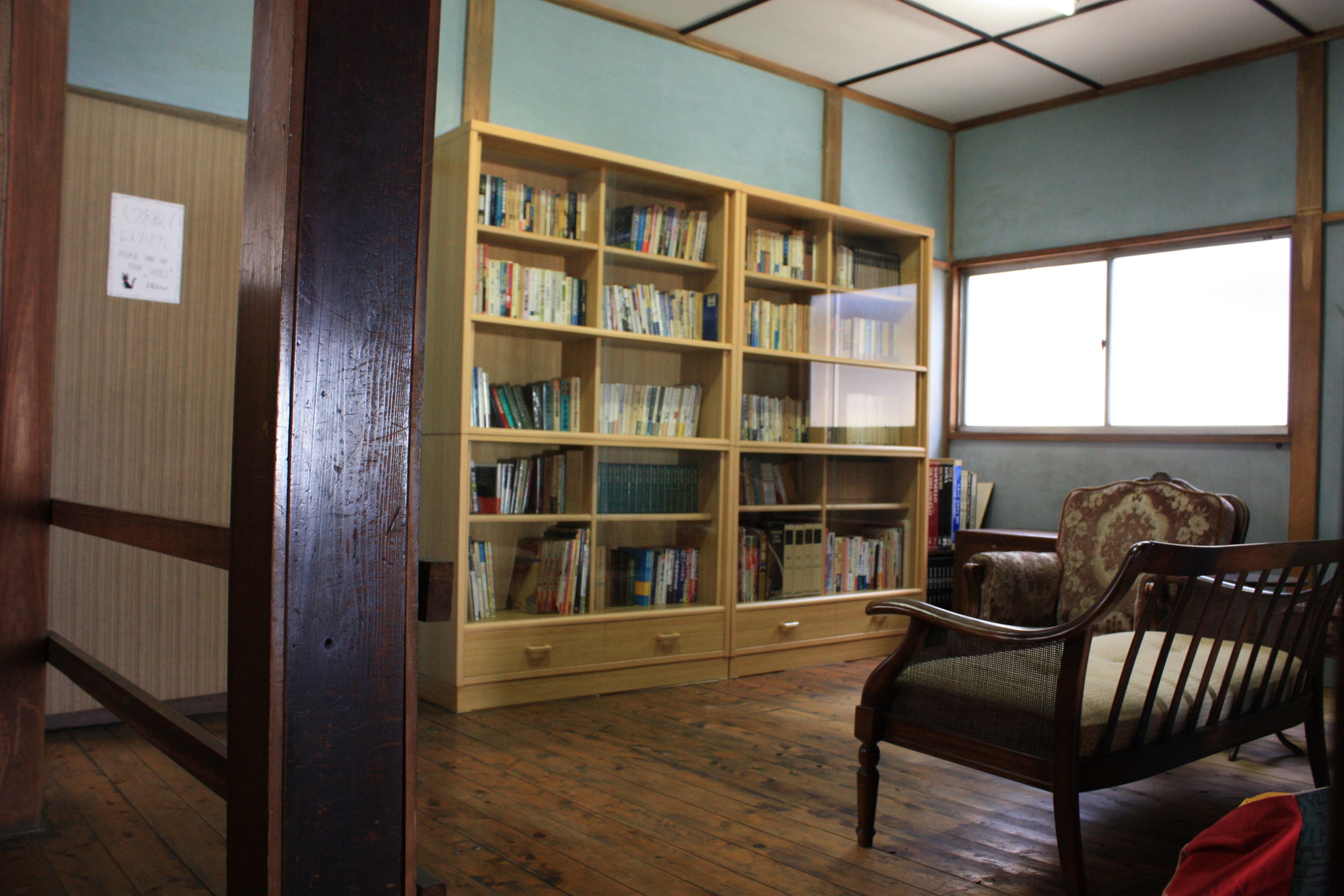 A room with a wooden bookshelf filled with books, a wooden chair, and a window.