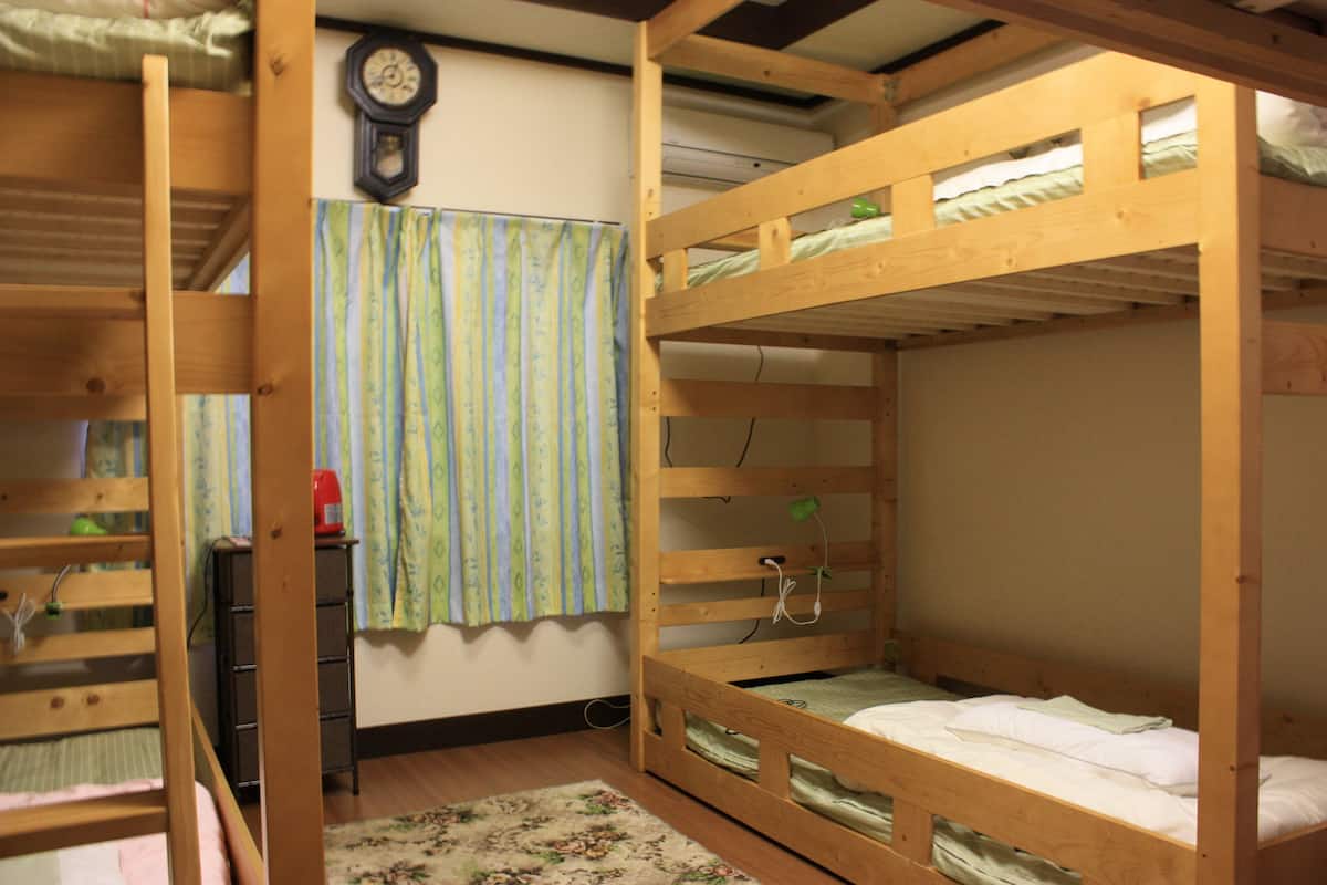 A bunk bed room with a wooden floor, a clock on the wall, and a curtain.