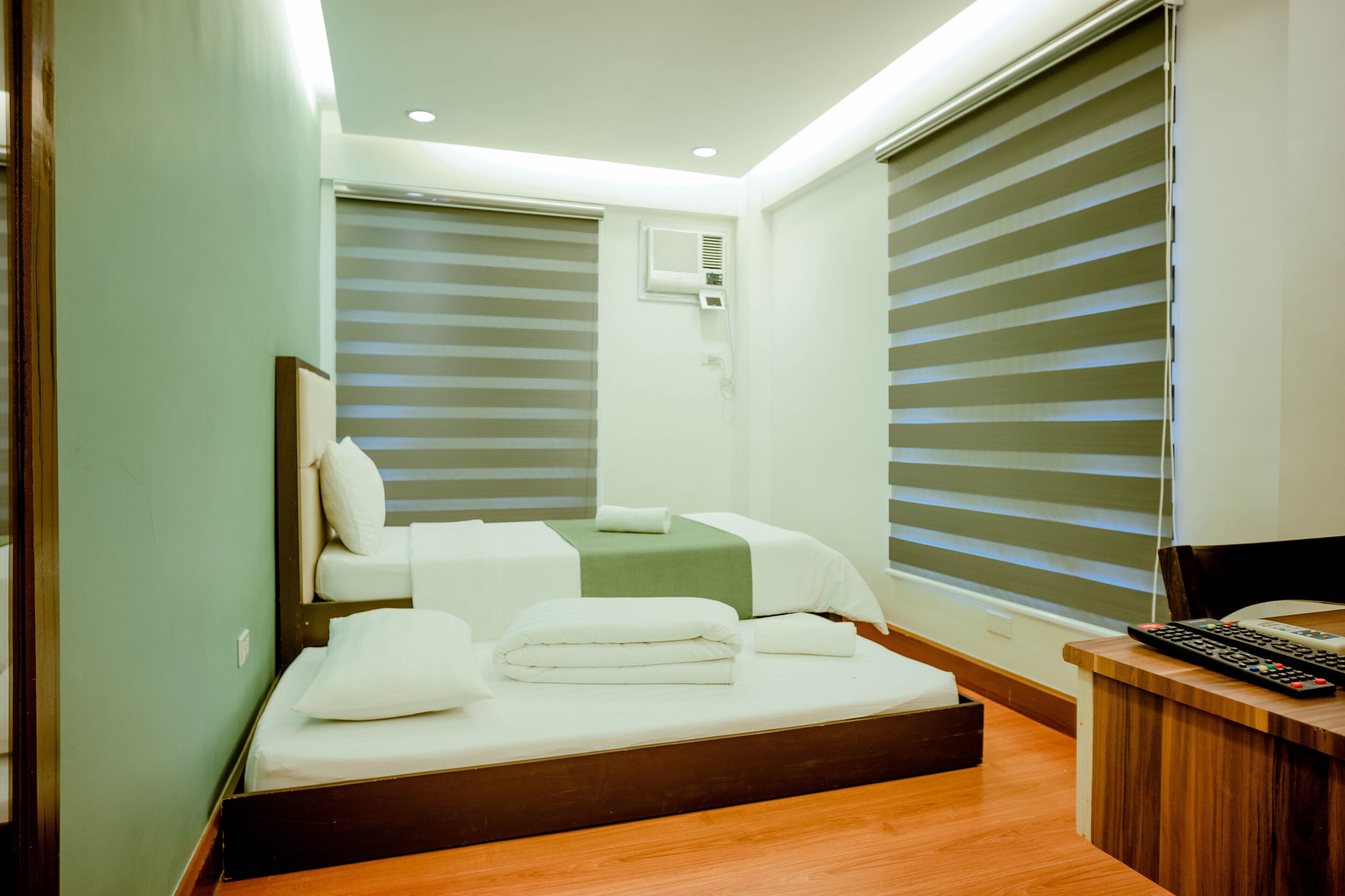 A modern hotel room with a bed, a desk, and a window with blinds.