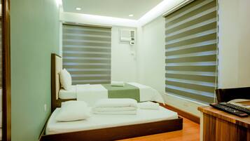 A modern hotel room with a bed, a desk, and a window with blinds.
