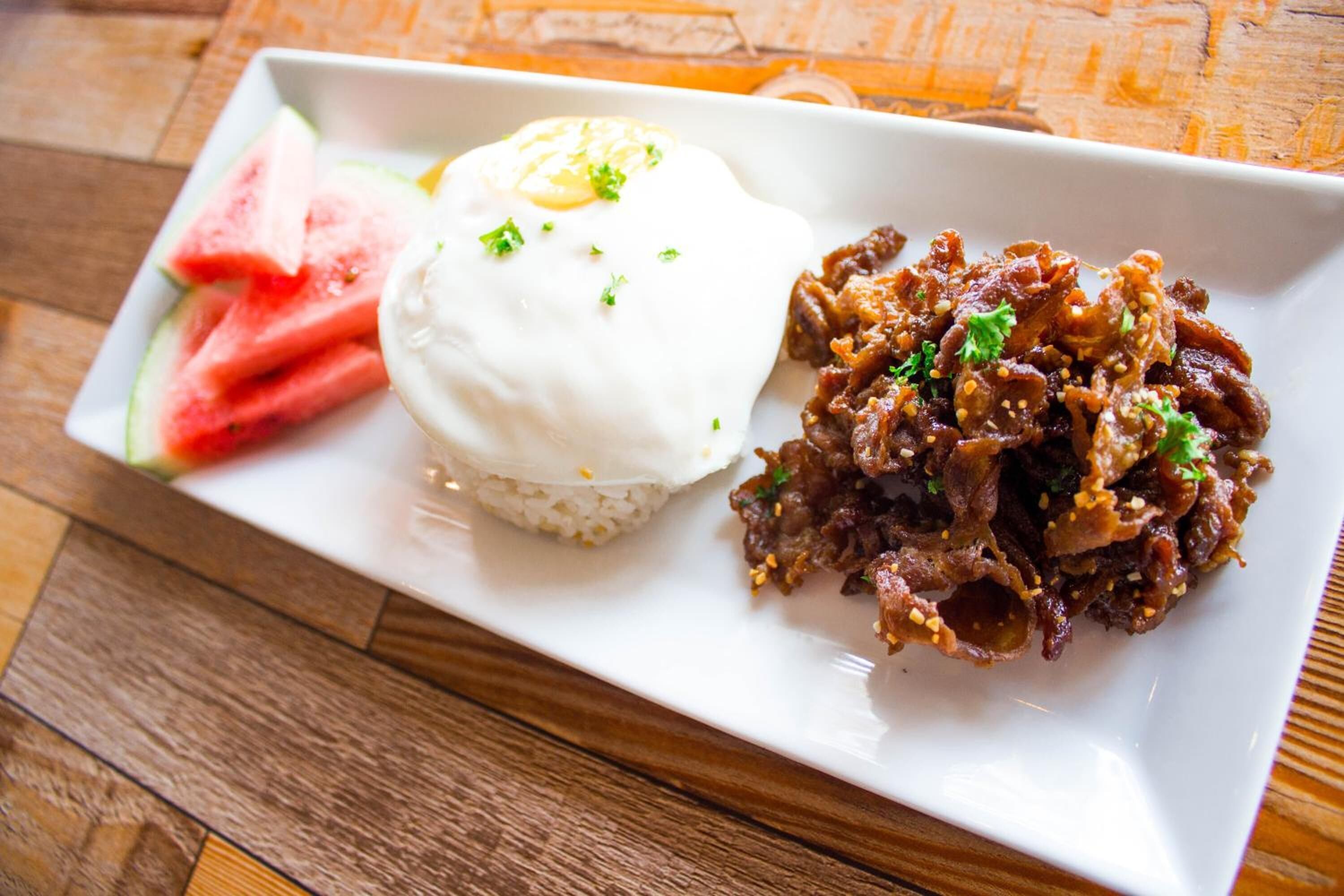 A plate with rice, a poached egg, and a meat dish, possibly beef, garnished with sesame seeds and herbs.