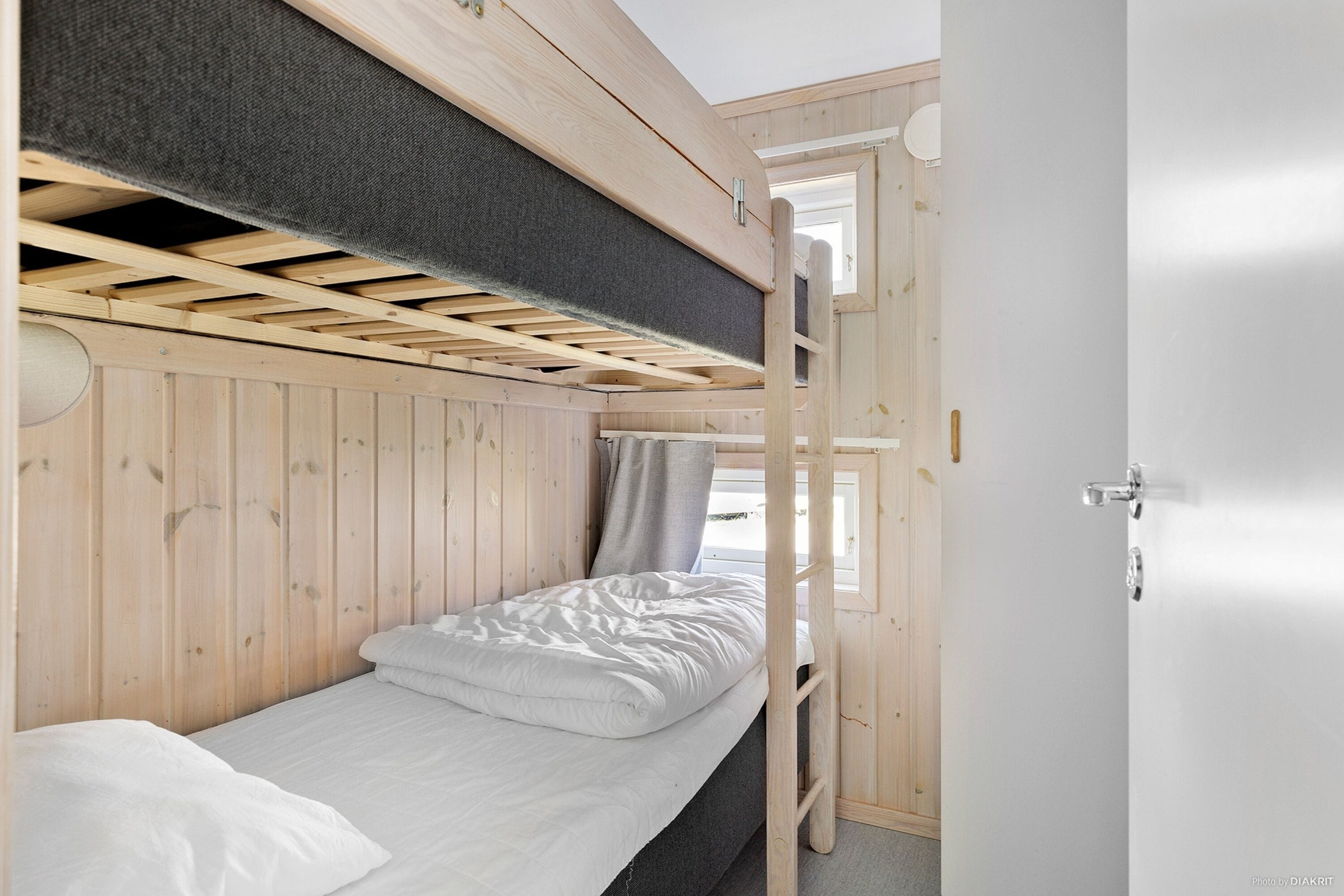 A bunk bed with a ladder, a window, and a door in a wooden room.