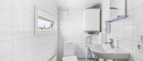 Une salle de bain moderne avec des carreaux blancs, des toilettes, un lavabo et une fenêtre.