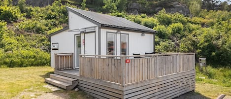 A small, single-story cabin with a sloped roof, a wooden deck, and a small porch.