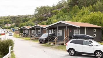 A row of cabins with wooden exteriors and tiled roofs, parked on a gravel path with a hilly backdrop.