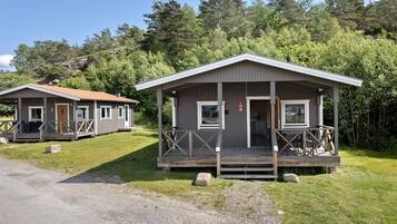 Two cabins with wooden decks and a porch, surrounded by greenery and a clear sky.