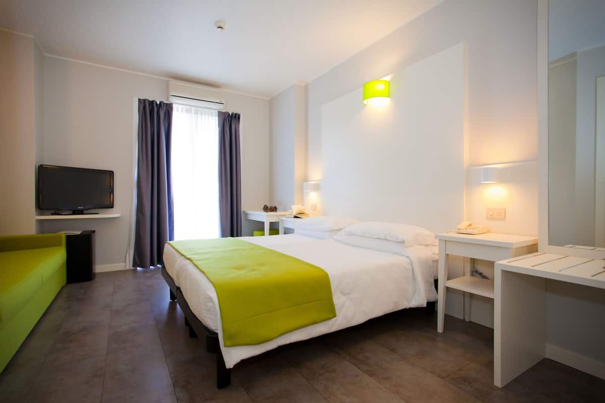 A hotel room with a bed, a desk, a chair, a TV, and a window with curtains.