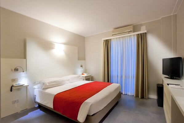 Una habitación de hotel con cama, mesitas de noche, televisor y aire acondicionado.