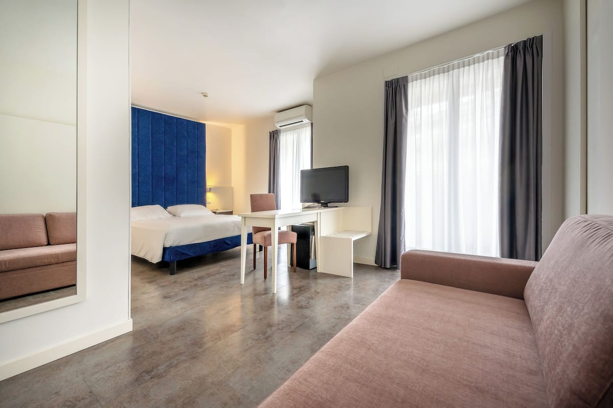 A hotel room with a bed, a desk, a television, and a sofa.