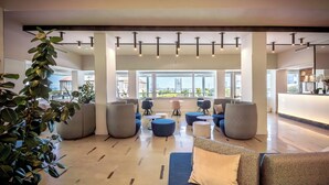 A spacious lobby with a modern design, featuring a large seating area with sofas and round tables, large windows offering views of the outside, and a clean, polished floor. - Hotel Garden Sea (Caorle)