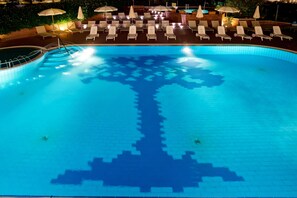 Una piscina con diseño de árbol en el suelo, rodeada de sillones de playa y sombrillas.
