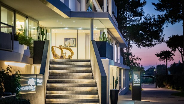 A modern building with a staircase leading to the entrance, surrounded by potted plants and a signboard. - Hotel Garden Sea (Caorle)