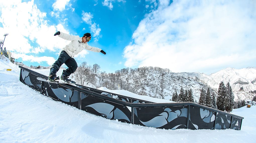 A snowboarder performing a trick on a rail in a snowy mountainous area.