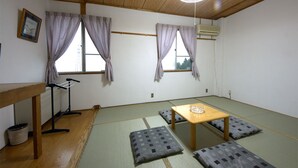 A room with tatami flooring, a low wooden table, cushions, a hanging clothes rack, and a ceiling fan. - Allumeur (Minamiuonuma)