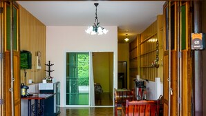A kitchen with wooden cabinets, a dining area with a wooden table and chairs, a chandelier, and a view through a glass door. - Chan De Bua (Chanthaburi)