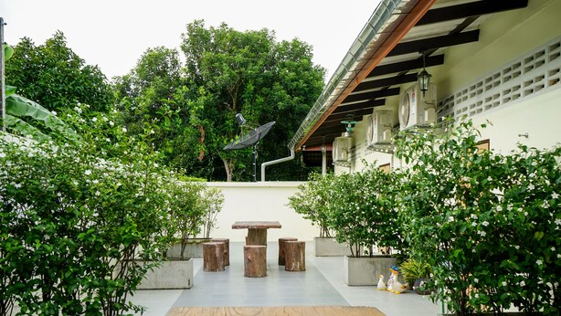 An outdoor patio area with a wooden table and benches, surrounded by potted plants and trees. - Chan De Bua (Chanthaburi)